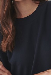 Navy blue short-sleeved top made of soft fabric, featuring a round neckline and a relaxed fit, with visible hair and skin tones.