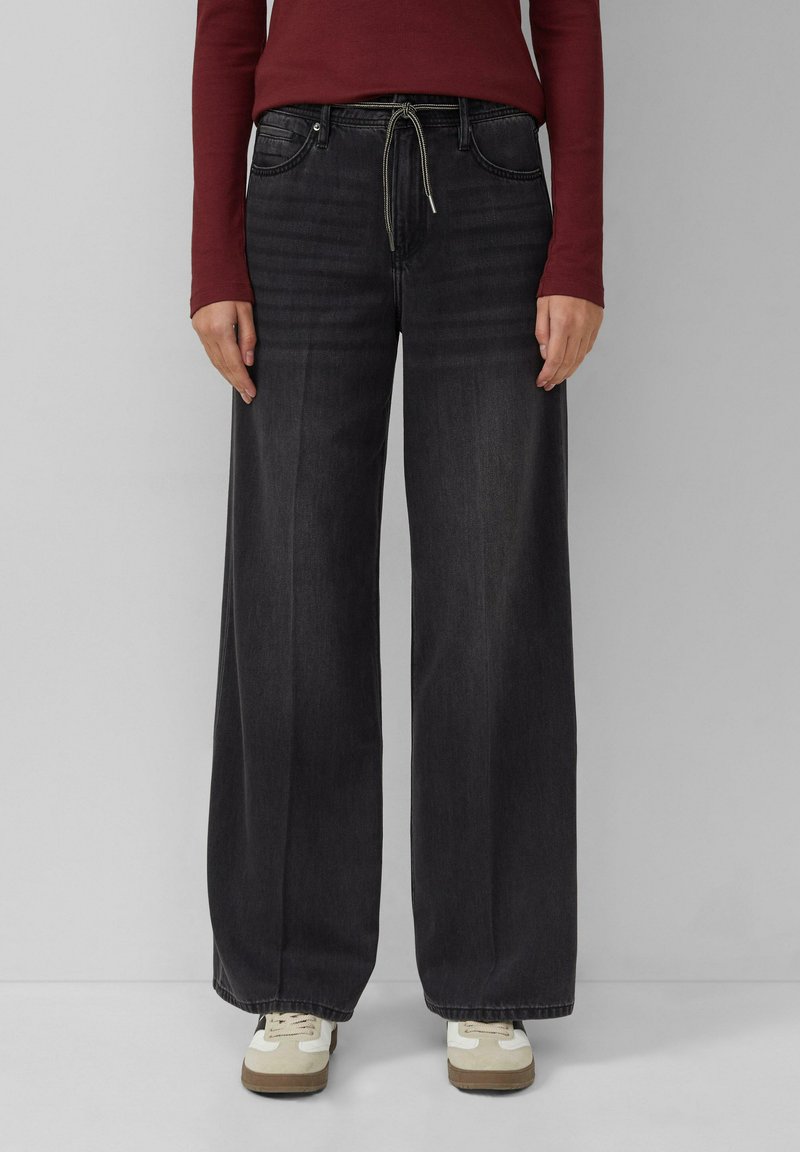 Schwarze weit geschnittene Jeans mit hoher Taille, ausgestattet mit Fronttaschen, einem Kordelzug und einer glatten Textur, kombiniert mit weißen Sneakers.