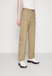 Khaki cargo-housut rentoa mallia, joissa on sivutaskut, vyölenkki ja sileä, kestävä puuvillakangas. Yhdistetty valkoisiin liukuhousuihin.