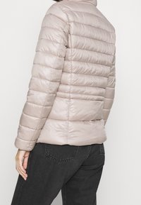 Padded, jasnoszara kurtka z poziomym przeszyciem, wysoki kołnierz i gładka tekstura, w połączeniu z ciemnymi dżinsami.