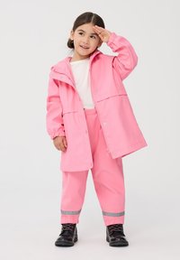 Różowa wodoodporna kurtka z kapturem, zapinana na napy i zamek, z elastycznymi mankietami. W połączeniu z dopasowanymi różowymi spodniami z odblaskowymi akcentami.