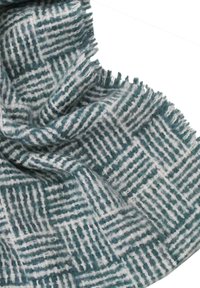 Manta texturizada en tonos verde azulado y blanco, con un patrón de cuadrícula. El material parece suave con bordes con flecos, añadiendo detalle y dimensión.