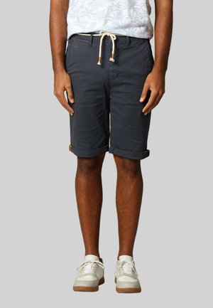 Shorts pour hommes gris foncé avec ourlets retroussés, en tissu coton, poches latérales et taille à cordon de serrage. Associés à des baskets blanches.