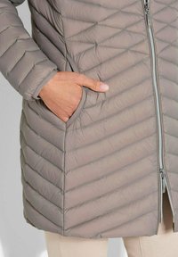Lichte, gequilt taupe jas met diagonaal stiksel, volledige ritssluiting en zijzakken. Zachte textuur en een slanke, fitted pasvorm.