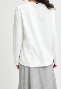 Maglia a maniche lunghe bianca con scollatura rotonda, realizzata in tessuto morbido. Presenta un taglio dritto con dettagli di cucitura discreti sul retro.