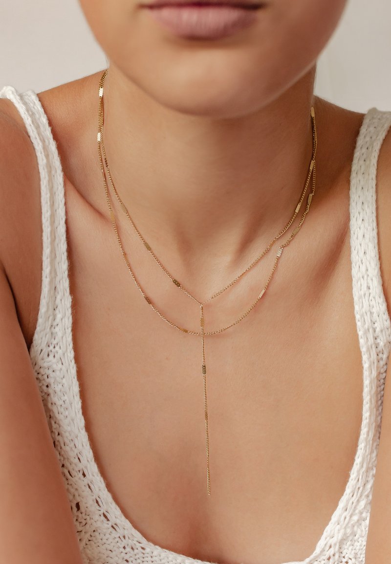 Naszyjnik o złotej powłoce składający się z trzech nici o różnych długościach, z małymi okrągłymi i prostokątnymi akcentami. Teksturalne ogniwa dodają szczegółów.