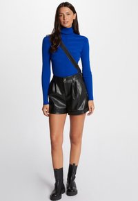 Blauer Rollkragenpullover mit gerippter Textur, kombiniert mit hochtaillierten schwarzen Leder-Shorts. Modell trägt schwarze Knöchelstiefel und eine Crossbody-Tasche.