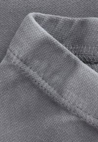 Close-up van opgevouwen grijze stof die de gebreide textuur en gedetailleerde stiksels langs de rand toont.