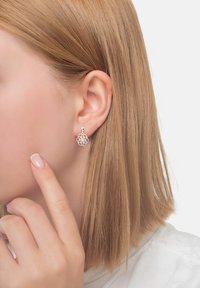 Orecchini a cerchio in argento con un intricato design geometrico, indossati da un modello con capelli lisci e castano chiaro.