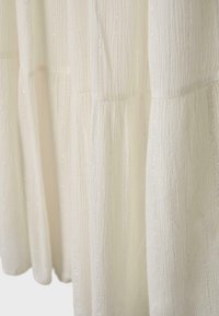 Gros plan d’un tissu blanc texturé présentant des lignes verticales et des détails subtils scintillants avec des coutures froncées.