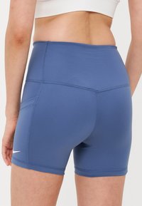 Shorts de sport bleus en matériau extensible, dotés d'une texture lisse, d'une taille mi-haute et d'un petit logo sur le côté.