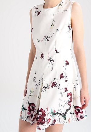Ærmeløs hvid kjole med en figursyet talje og en udvidet nederdel, der har et blomsterprint i nuancer af rød, pink og grøn.