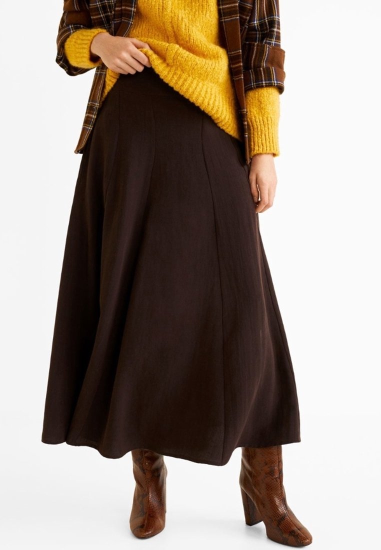 Jupe maxi marron, fluide, avec une texture lisse, associée à un gros pull jaune et des bottes à talons marron à motifs.