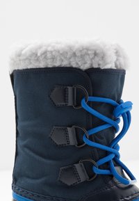 Granatowe śniegowce z kołnierzem z polaru, teksturowanym materiałem, niebieskim systemem sznurowania i sześciokątnymi oczkami zapewniającymi pewne dopasowanie.