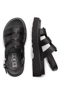 I sandali neri in pelle presentano molteplici cinturini intrecciati, una soletta imbottita e una parte inferiore tassellata per una presa extra. Compresa una cinghia per la caviglia regolabile.