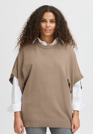 Beige, oversized sweater med korte ærmer, ribbet krave og kant, lagd over en hvid skjorte. Lavet af strikket stof, glat tekstur.