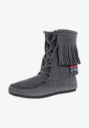 Stivale in camoscio grigio con parte superiore frangiata, chiusura frontale con lacci, dettagli decorativi perline rosse e blu, e suola testurizzata.