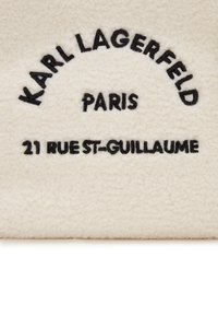 Cream-colored, fleece fabric with black embroidered text: "KARL LAGERFELD PARIS 21 RUE ST-GUILLAUME." Soft texture, rounded shape.
