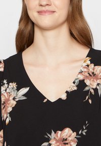 Vestido preto com decote em V, apresentando padrões florais em tons de pêssego e branco. Tecido macio e texturizado com mangas curtas.