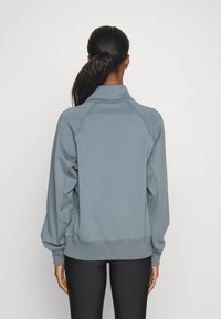 Blå sweatshirt med hög krage, raglanärmar och ribbad nederkant. Tillverkad av mjukt material med en slät yta.