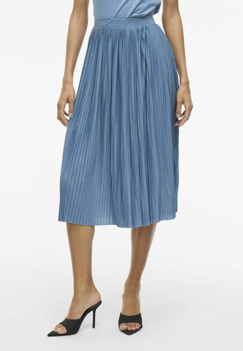 Plisovaná midi sukňa vo svetlomodrej farbe, s priliehajúcim pásom a hladkou textúrou. V kombinácii s čiernymi opätkovými sandálmi.