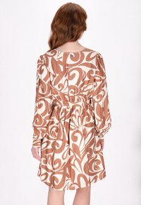 Braun- und cremefarbenes gemustertes Kleid mit langen Ärmeln, tailliertem Schnitt und rundem Halsausschnitt, das wellenförmige Designs und eine weiche Stoffstruktur zeigt.