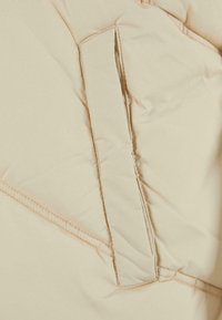 Tela de chaqueta de plumas beige con un patrón de costura diagonal; cuenta con un bolsillo con solapa de textura suave y costura reforzada.