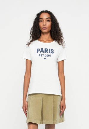 T-shirt blanc avec inscription navy "PARIS EST. 2007" et une petite icône de cœur, associé à une jupe plissée en velours côtelé vert olive clair.