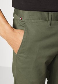 Olivegröna chinos i bomull med en mjuk textur. Har en sidficka och en liten röd, vit och blå logotypaccent på midjebandet.