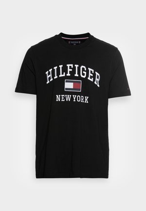 T-shirt nera a maniche corte con "HILFIGER" e "NEW YORK" in testo bianco e un logo rettangolare rosso, bianco e blu centrato sul petto.