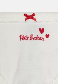 Vita bomullsunderkläder med röd broderad text "Petit Bateau", två små röda hjärtan och ett dekorativt rött band vid midjan.