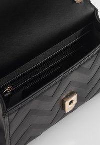 Borsa nera con texture a chevron e chiusura in metallo dorato. L'interno presenta una tasca con zip e diversi slot per carte. Finitura in materiale liscio.