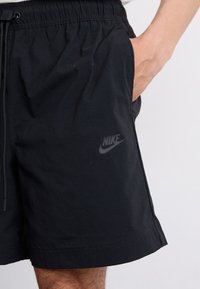 Black Nike shorts with an elastic waistband, side pockets, and a subtle logo on the left leg. Smooth fabric texture, mid-thigh length.