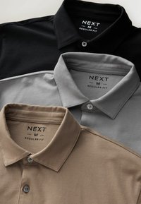 Drei Poloshirts in Schwarz, Grau und Beige übereinander gestapelt. Jede hat einen Kragen und eine Knopfleiste mit den "NEXT M REGULAR FIT"-Labels.