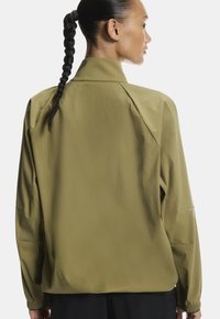 Olajzöld, könnyű dzseki magas gallérral, hosszú ujjakra és laza szabásra tervezve. Simább textúra, finom varrási részletekkel és logóval.