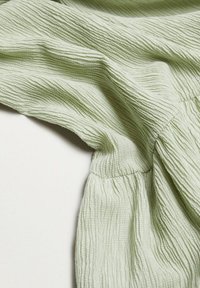 Gros plan d'un tissu vert clair texturé avec des coutures froncées et des stries verticales sur une surface douce et froissée.
