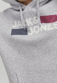 Felpa grigia con cappuccio, dotata di tasca frontale e la scritta "JACK & JONES." Include dettagli a righe in blu navy e bordeaux. Tessuto morbido.
