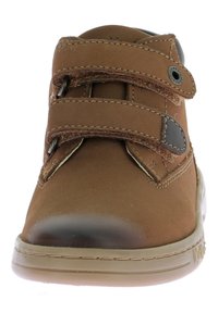 Zapato de cuero marrón con dos correas ajustables, puntera redondeada y suela de goma. Presenta detalles de costura y un botón metálico circular.