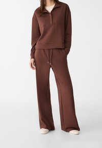 Brun sweatshirt med en kvart dragkedja och breda ärmslut, kombinerad med matchande lösa byxor. Båda tillverkade av mjukt, slätt tyg.