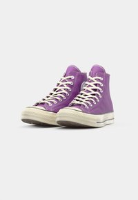 High-top sneakers in vibrant purple canvas with white laces, rubber toe cap, and a textured cream sole; features classic logo patch on side.