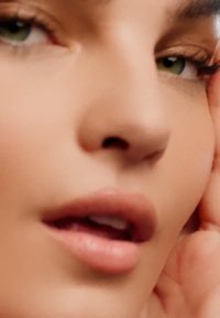 Nærbilde av et ansikt med glatt hud, godt definerte kinnben, fyldige lepper og grønne øyne. Naturlig sminke fremhever trekkene.