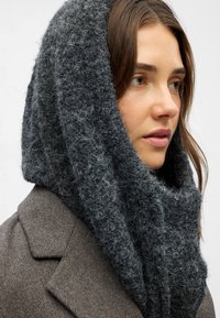 Chunky gray knit scarf made from soft, textured material, draped loosely around the neck, with a cozy, voluminous design and a close-up view.