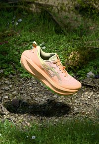 Lightweight running shoe in peach and green, featuring a breathable mesh upper, cushioned sole, and textured surface for traction.