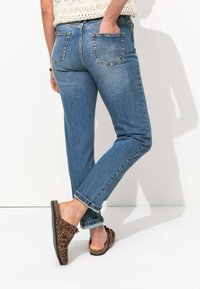 Jeans en denim bleu clair à coupe décontractée, avec cinq poches et ourlets roulés. Portés avec des chaussures à enfiler à motif léopard marron.