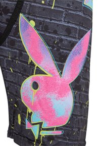 Shorts en tissu noir avec un grand logo de lapin rose et bleu, sur un fond de motif en briques grises texturé avec des éclaboussures jaunes vives.