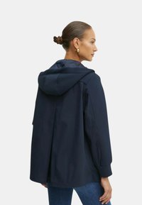 Giacca con cappuccio blu navy dal taglio morbido, maniche lunghe e dettaglio di apertura sul retro. Tessuto liscio e senza chiusure visibili.