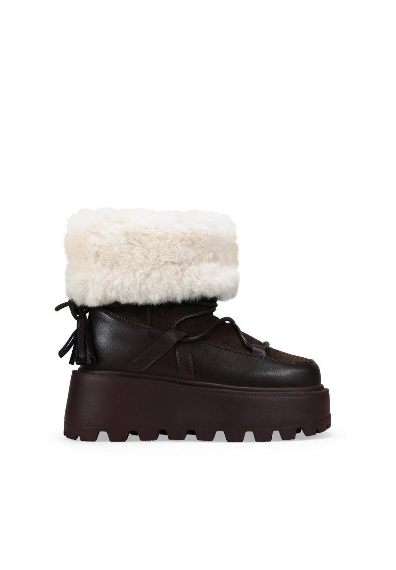 Botas de plataforma marrones con un dobladillo de borreguito, que presentan un diseño con cordones y materiales texturizados, destacando un estilo moderno y robusto.