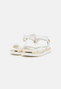 Białe sandały z syntetycznym wierzchem, regulowanymi paskami, platformą oraz złotymi akcentami wzdłuż krawędzi. Z tyłu zamknięte.