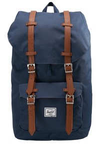 Sac à dos bleu marine avec des sangles en cuir marron et des boucles argentées, poche avant et étiquette de la marque Herschel sur le bas devant.