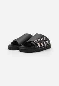 Sandale negre, tip slip-on, fabricate din piele netedă, cu accente din catarame argintii și un toc zimțat pentru aderență.